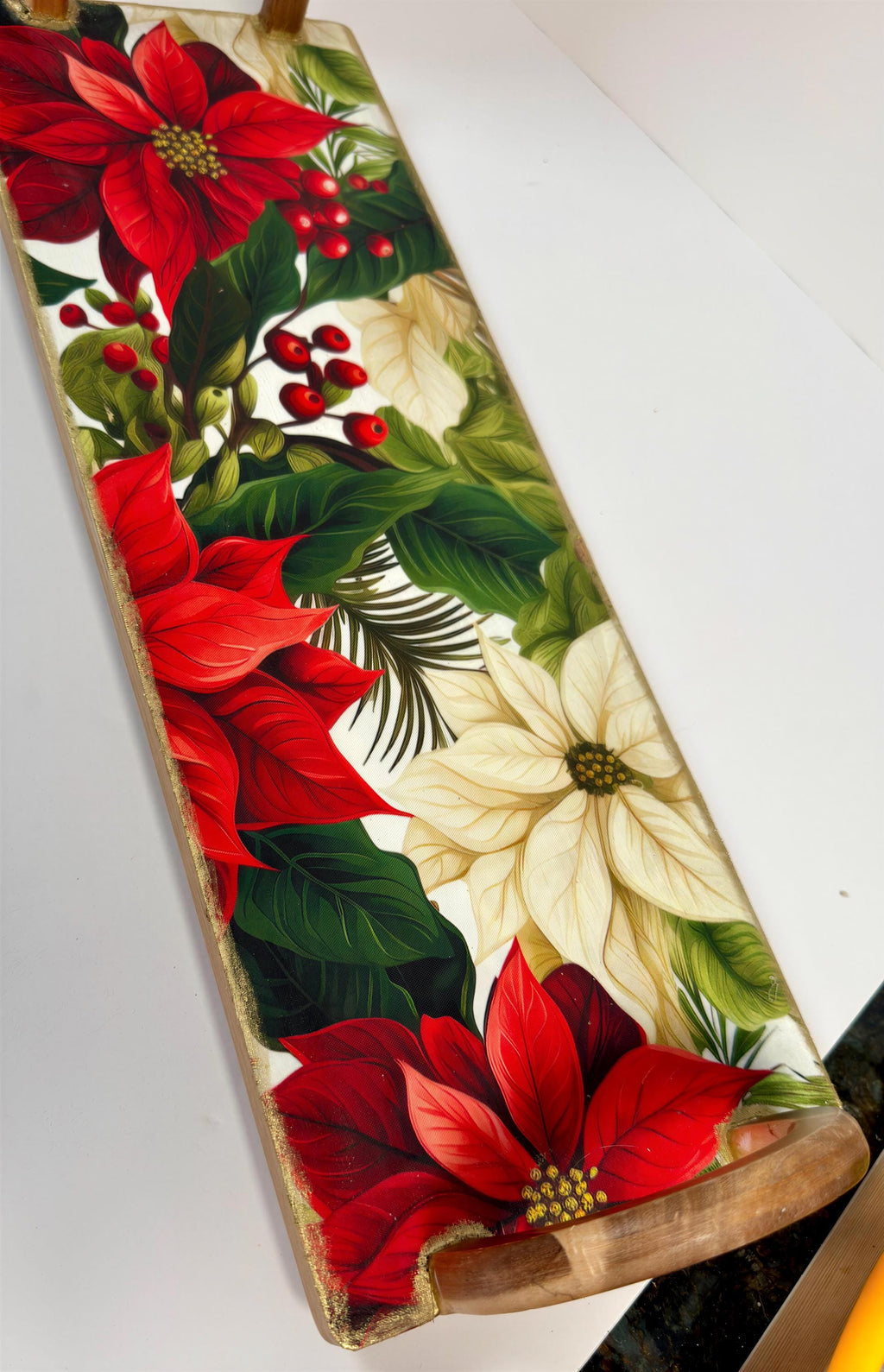 a wooden tray with a vibrant floral design, including red poinsettia flowers, green leaves, and white flowers.