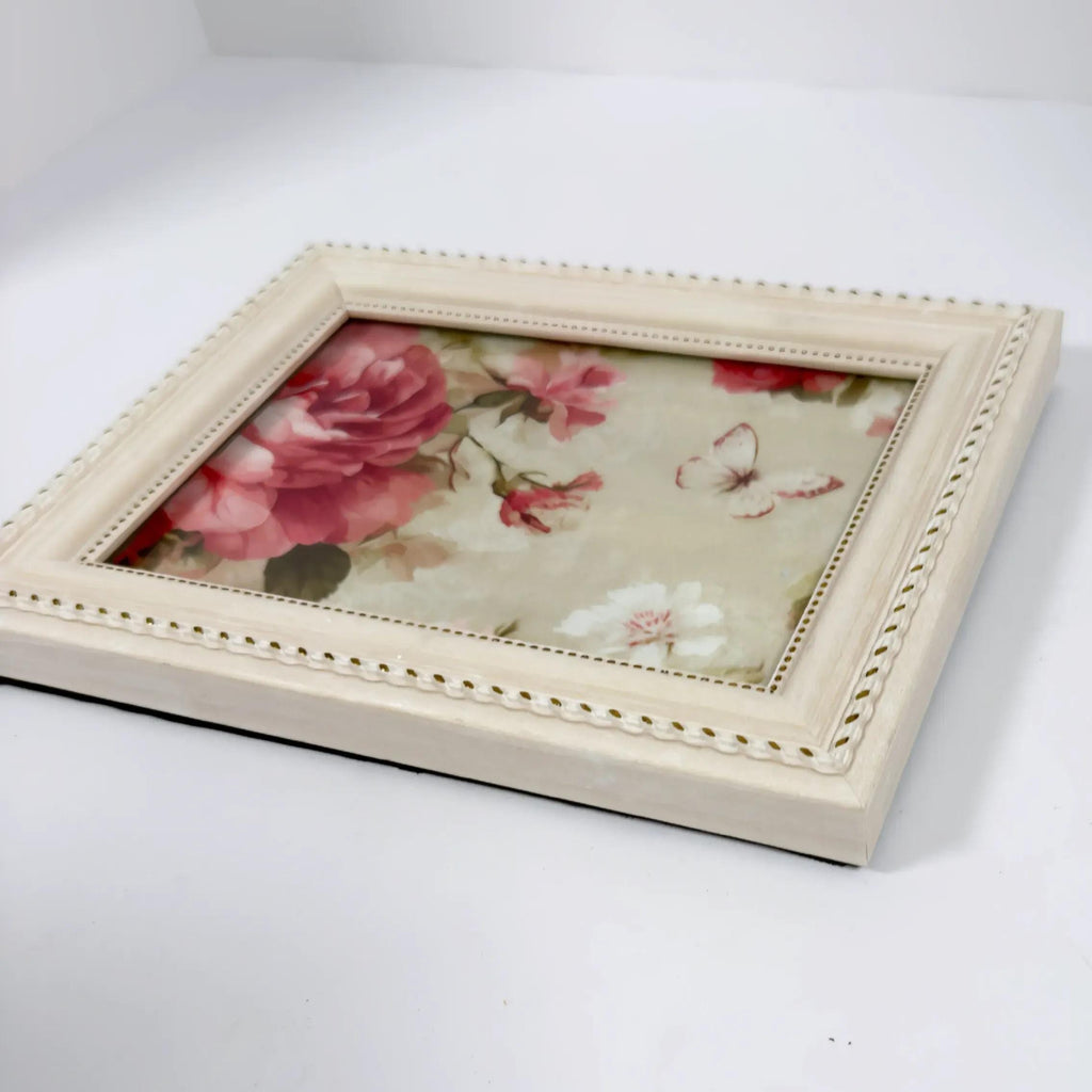 A white wooden frame with a floral print inside, placed on a white surface.