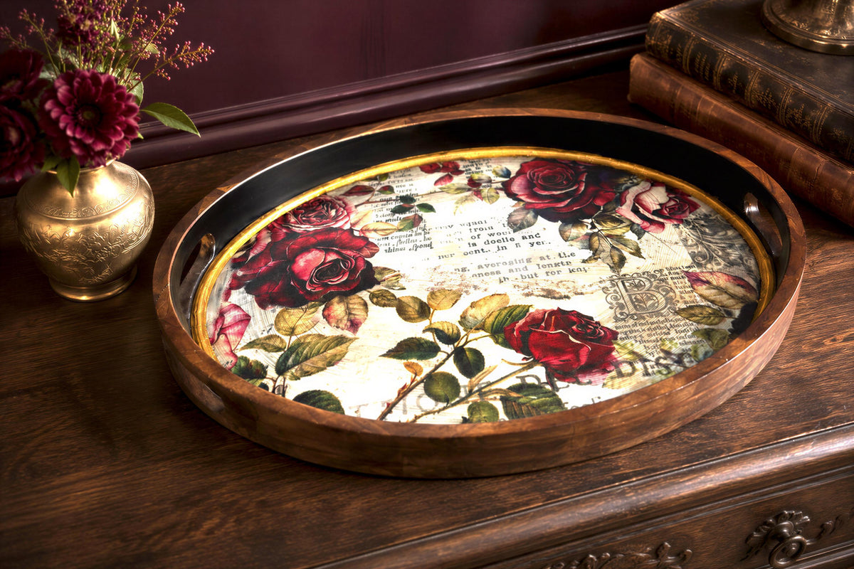 a wooden tray with a floral design, placed on a wooden surface next to a vase of flowers and some books.