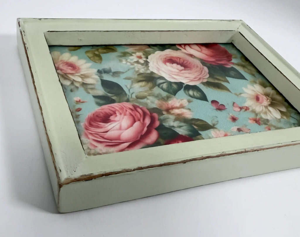 A wooden frame with a floral pattern of pink roses and other flowers inside it.