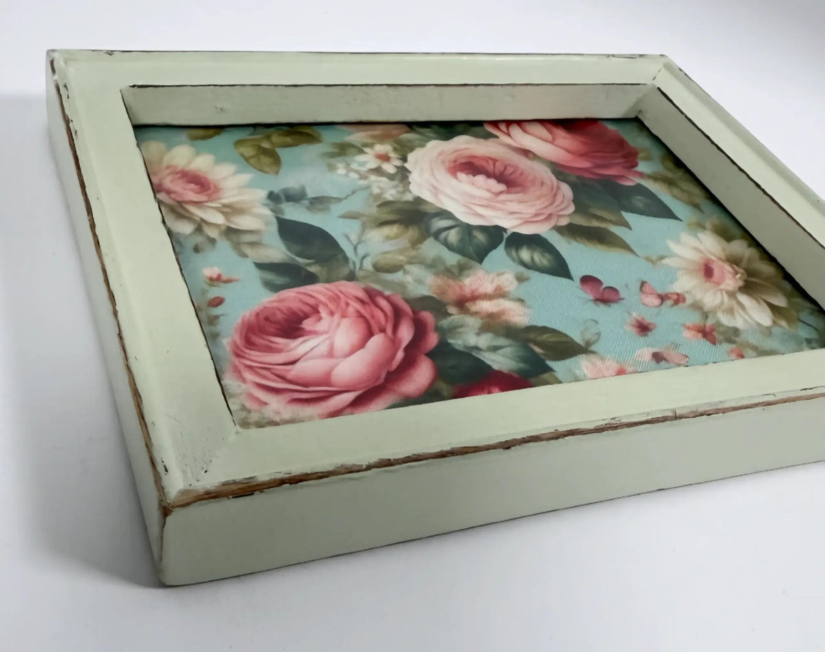 A wooden frame with a floral pattern of pink roses and other flowers inside it.