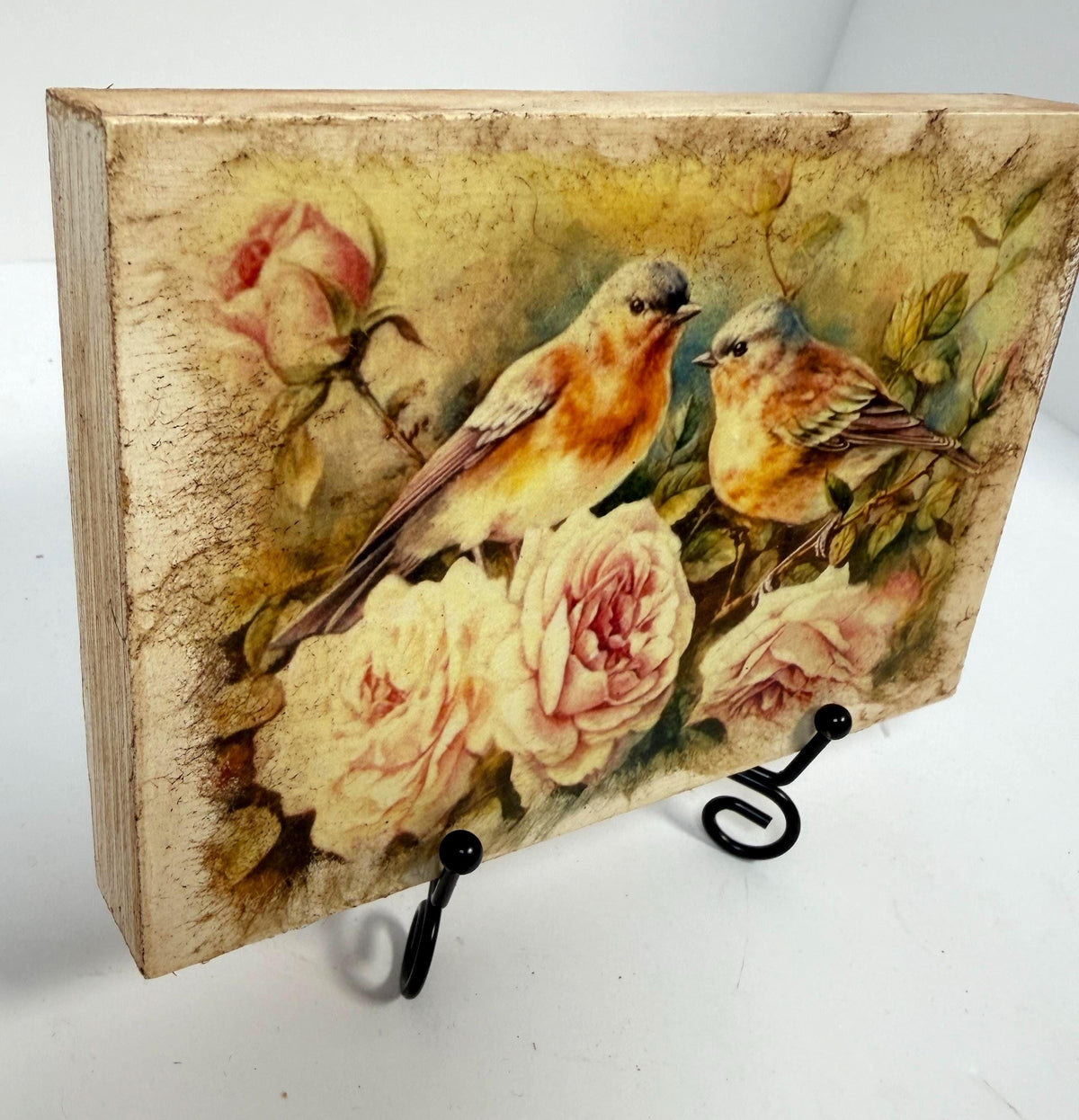 a wooden block with a painting of two birds perched on flowers, including roses.