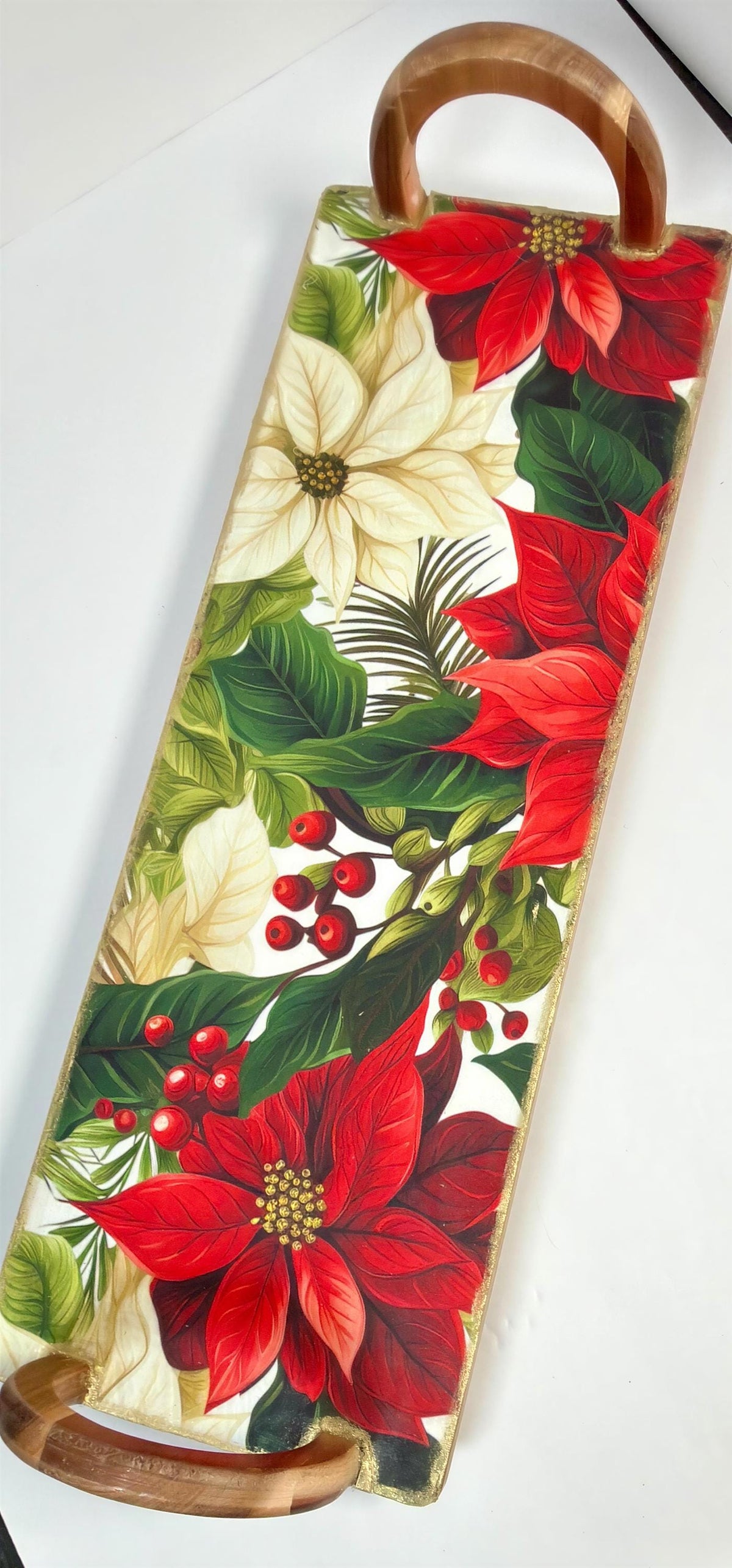 A wooden tray with a floral design featuring red poinsettia flowers, green leaves, and red berries.