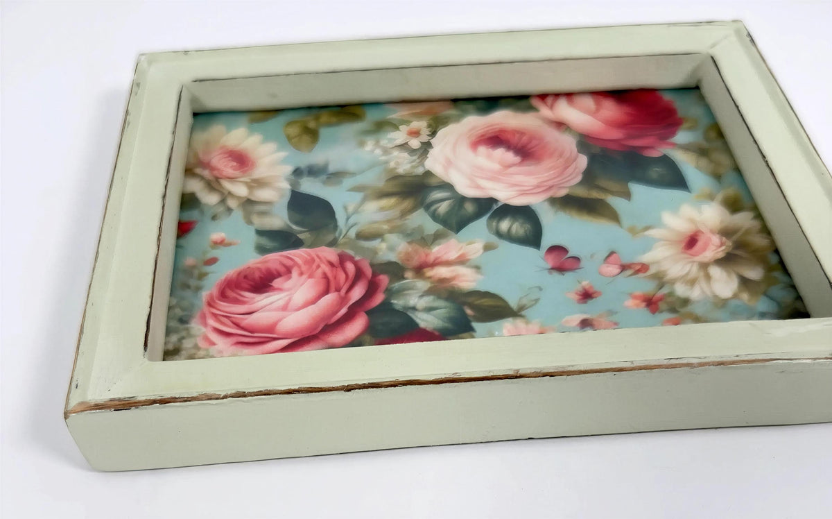 A wooden frame with a floral pattern of pink roses and other flowers inside it.