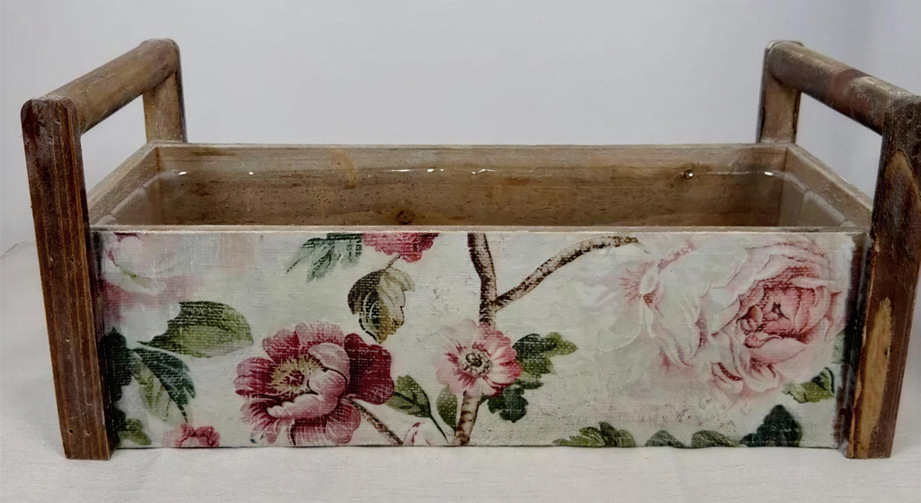 A wooden box with a floral pattern on its side, featuring pink and white flowers and leaves.