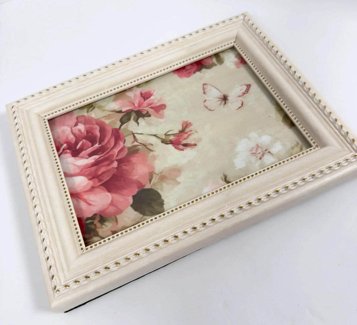 A white picture frame with a floral design inside, featuring a large pink rose and a butterfly.