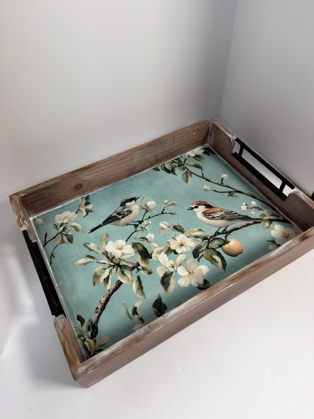 A wooden tray with a floral pattern of white flowers and green leaves, featuring two small birds perched on branches.