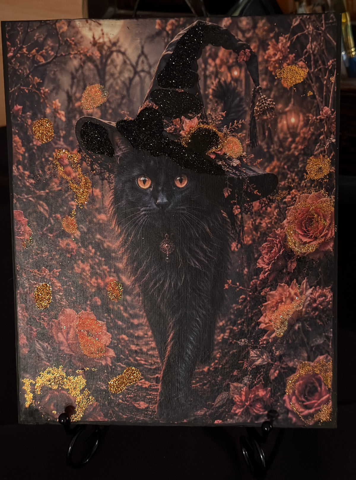 A black cat wearing a witch's hat, surrounded by a forest of flowers and foliage, creating a whimsical and enchanting scene.