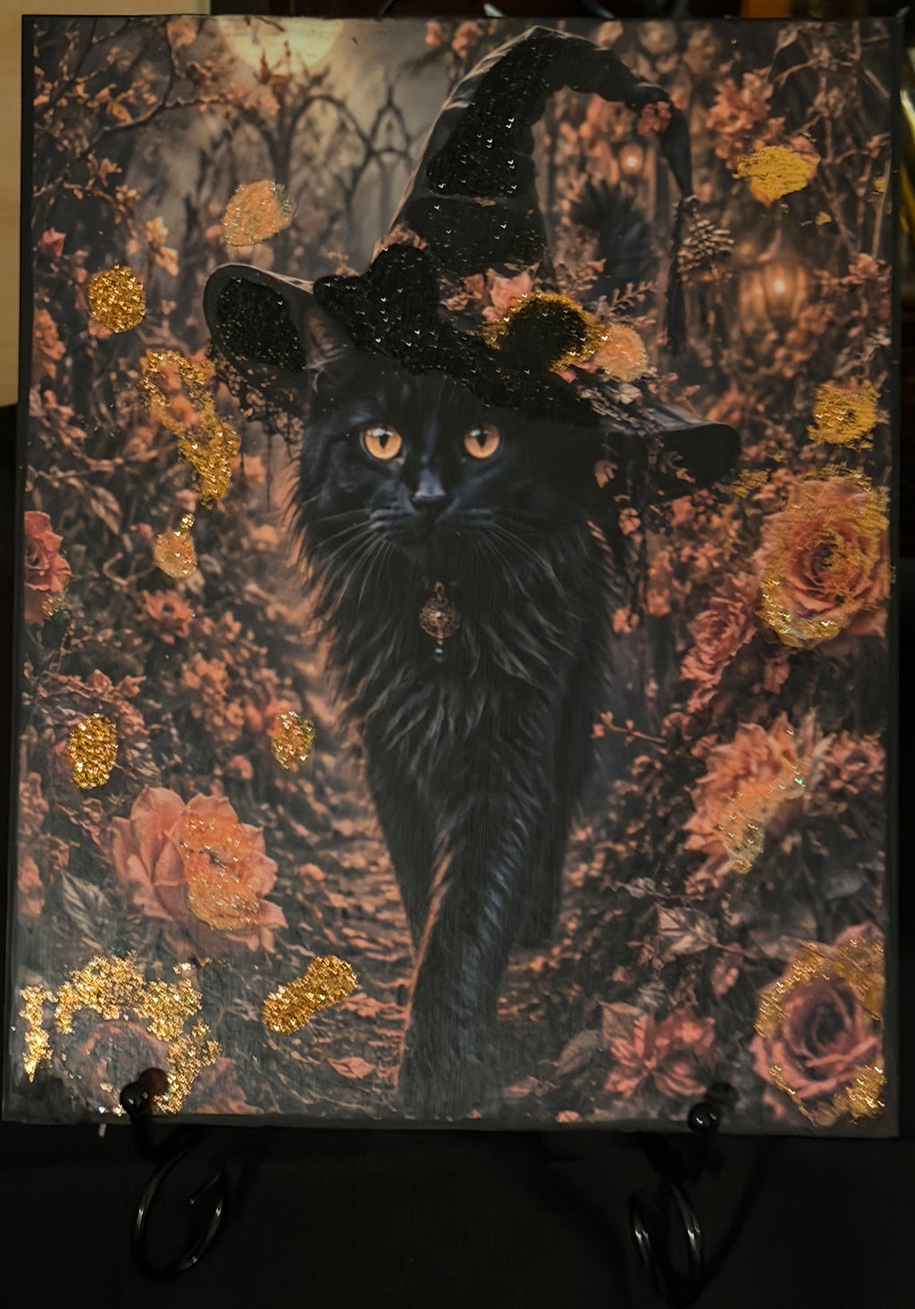 A black cat wearing a witch's hat, surrounded by a colorful autumnal scene with flowers and foliage.