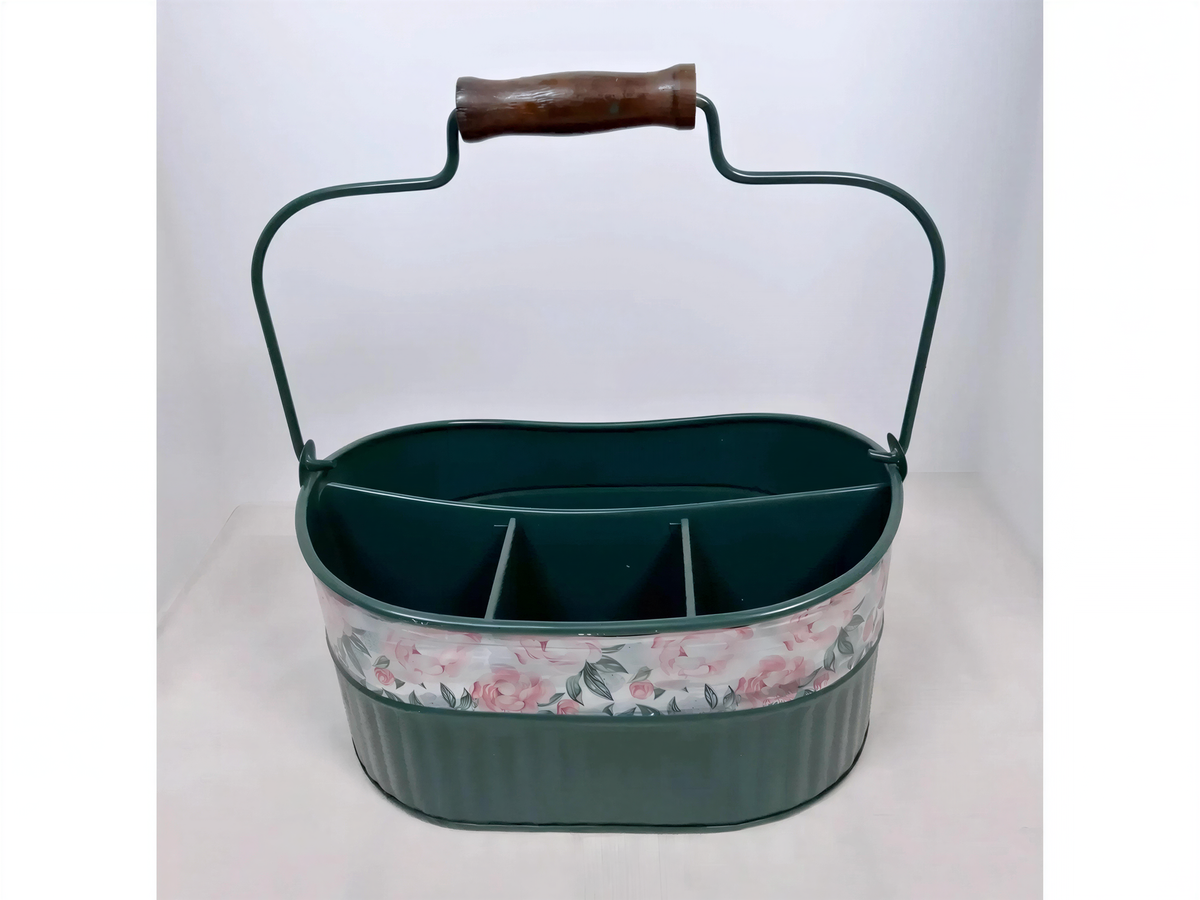A green metal basket with a floral pattern on the front, featuring a handle and divided compartments.