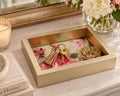 A gold-framed tray on a white marble countertop holds a keychain, a ring, and a small bowl, with a vase of white flowers and a candle nearby.
