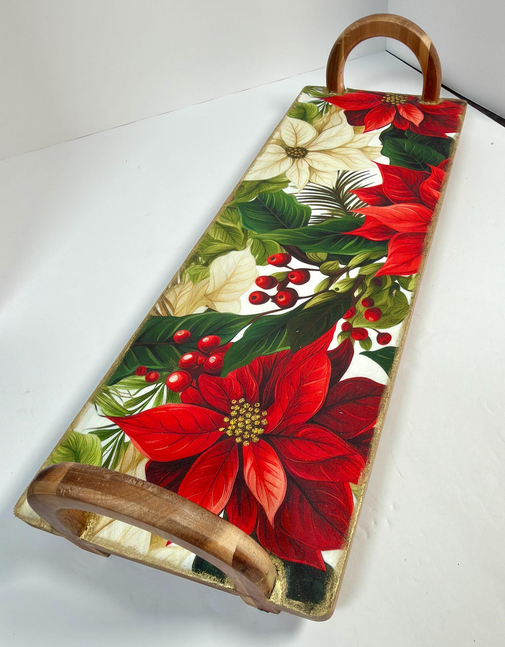 a wooden tray with a vibrant floral design, including red poinsettia flowers, green leaves, and red berries.