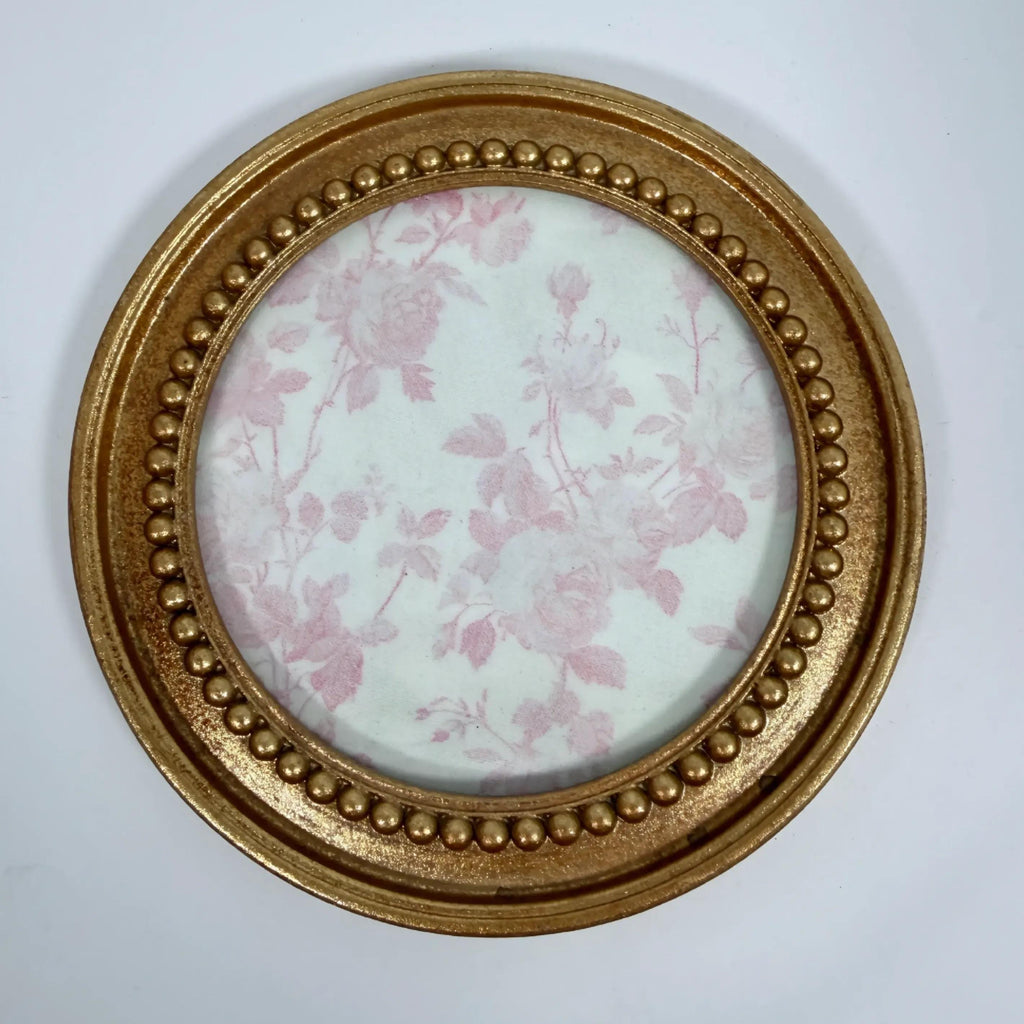 a round gold-colored frame with a floral pattern on the inside, set against a white background.