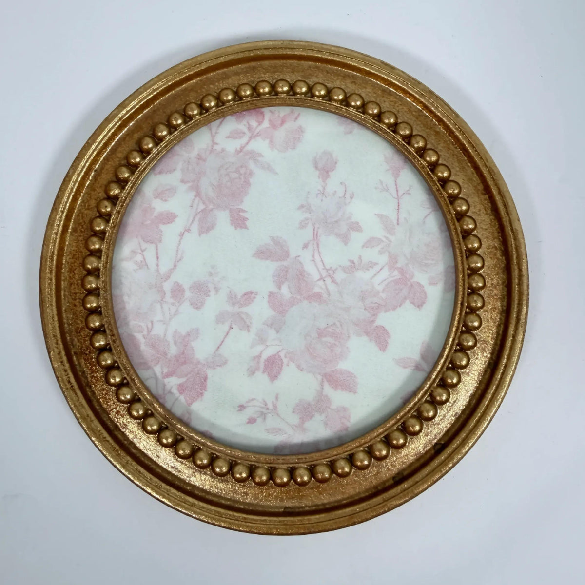 a round gold-colored frame with a floral pattern on the inside, set against a white background.