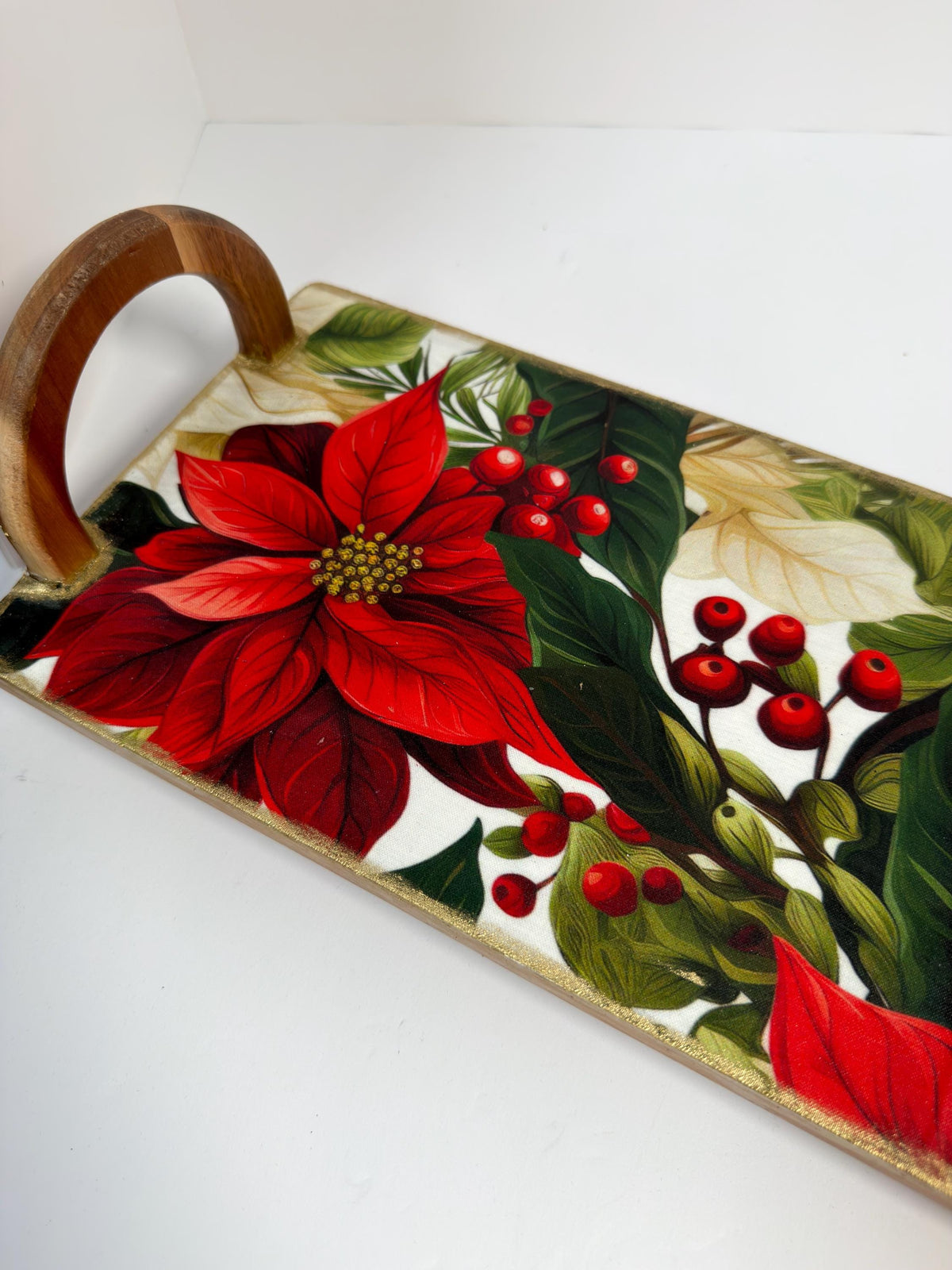 a wooden tray with a vibrant floral design, including a large red poinsettia flower surrounded by green leaves and red berries.