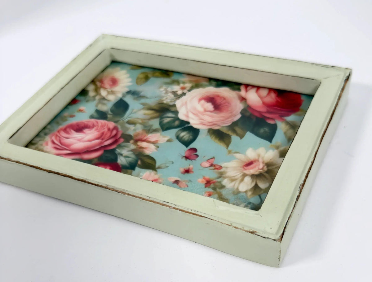 A framed picture of a floral design with pink roses and other flowers.