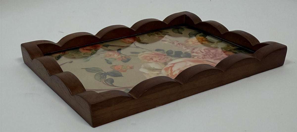 A wooden tray with a scalloped edge and a floral pattern on the front.