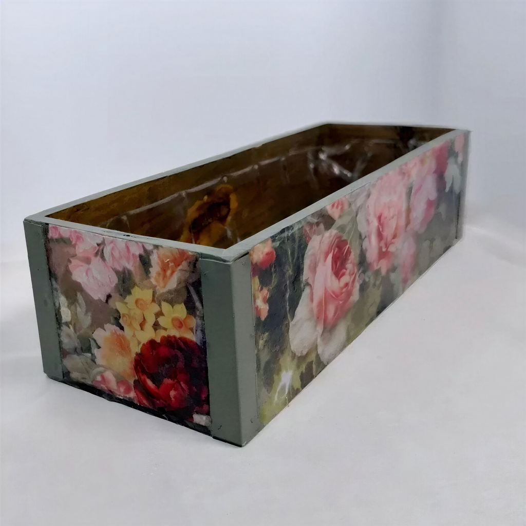 A rectangular wooden box with a floral pattern on its side, sitting on a white surface.