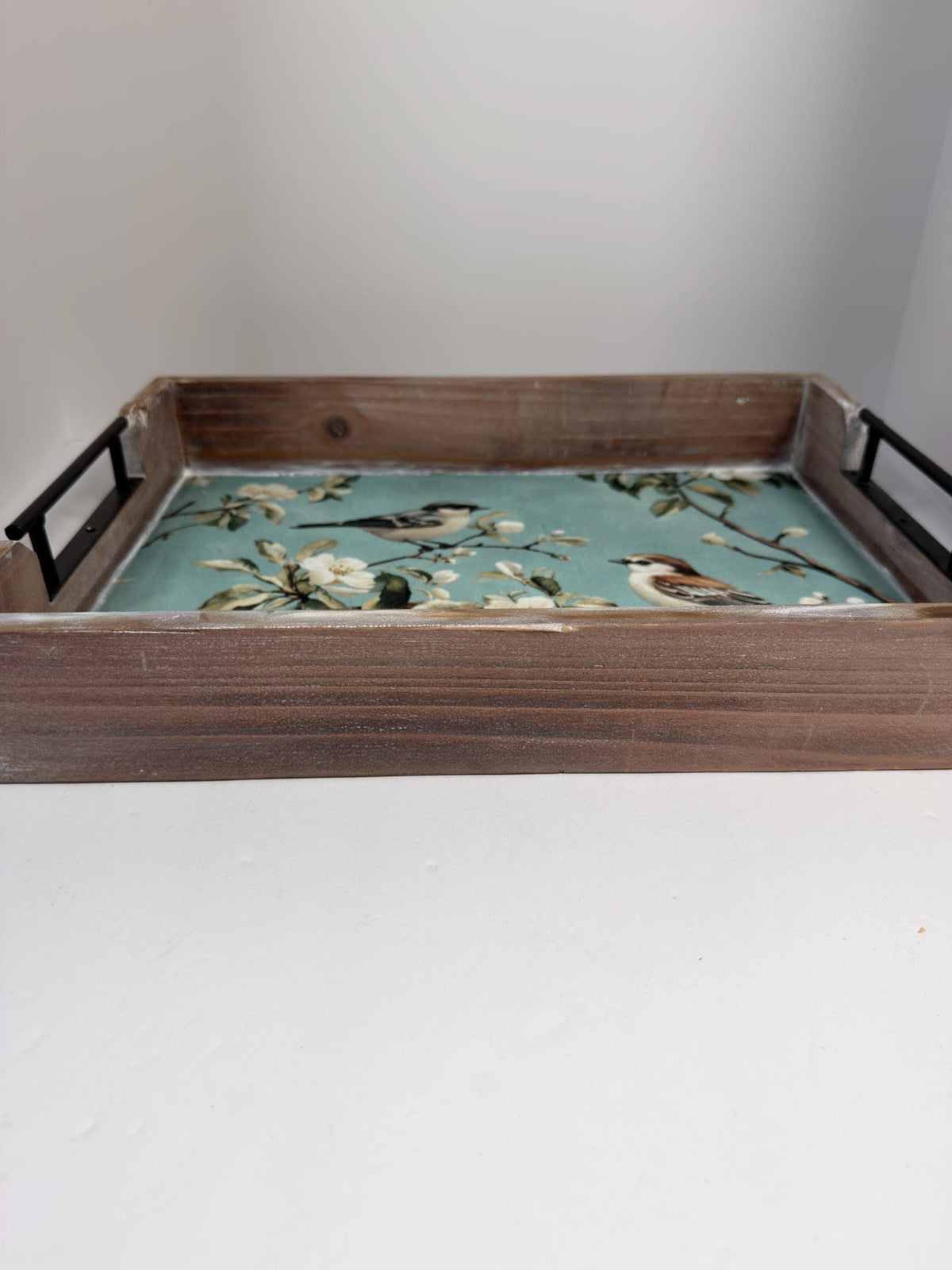 A wooden tray with a blue floral pattern on it, placed on a white surface.