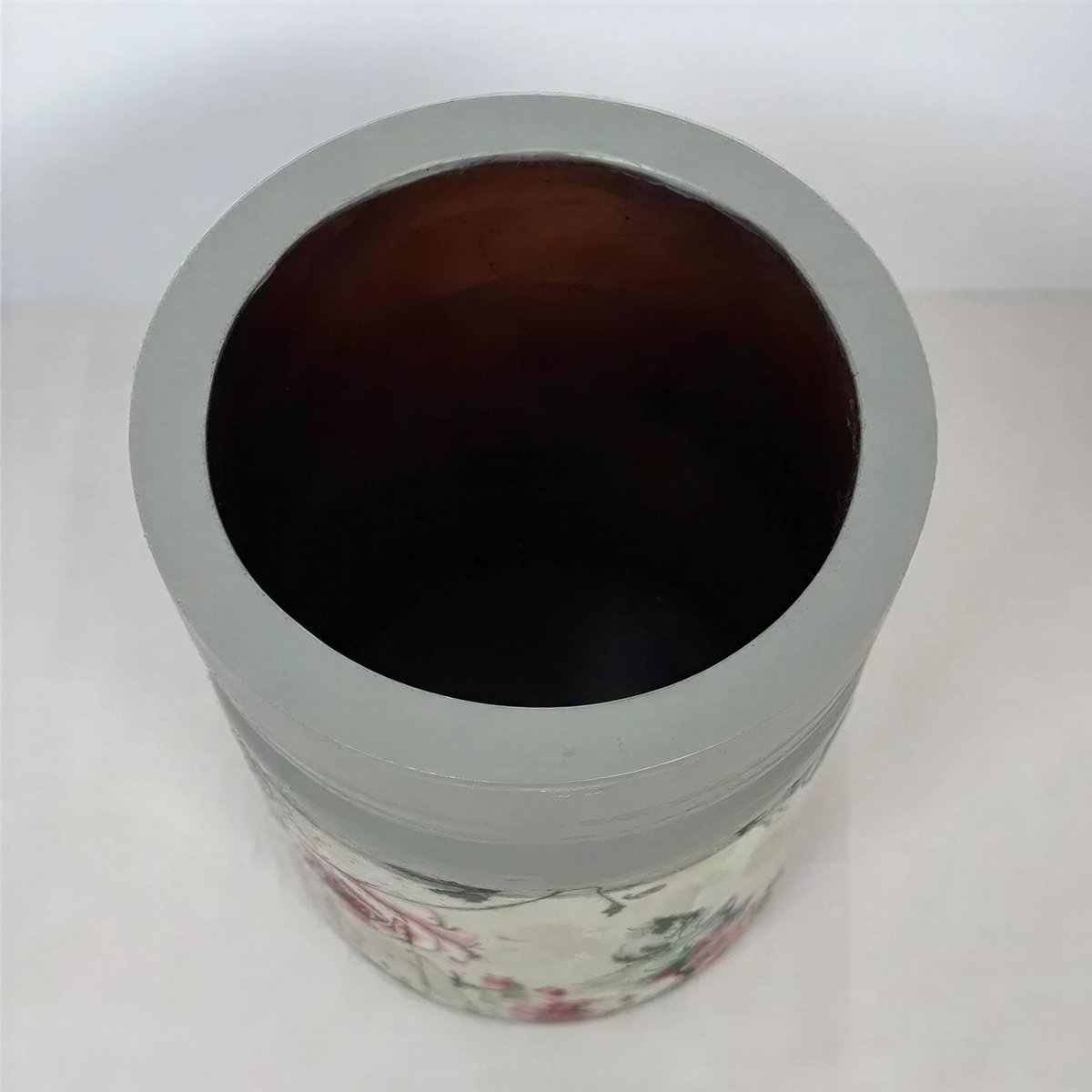 A gray vase with a floral pattern on it, sitting on a white surface.