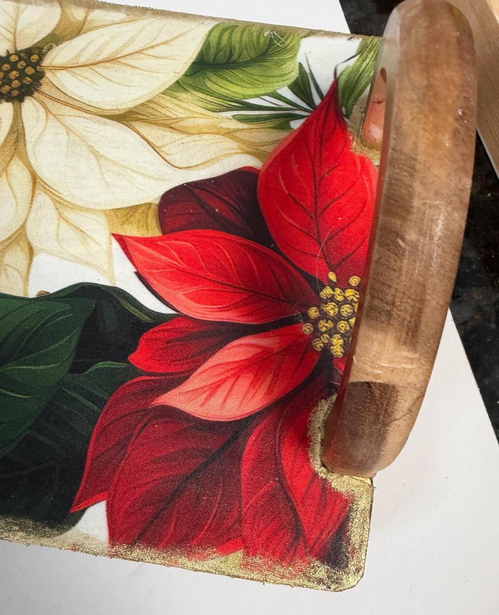 a close-up view of a wooden tray with a vibrant floral design, including red poinsettia flowers and green leaves.