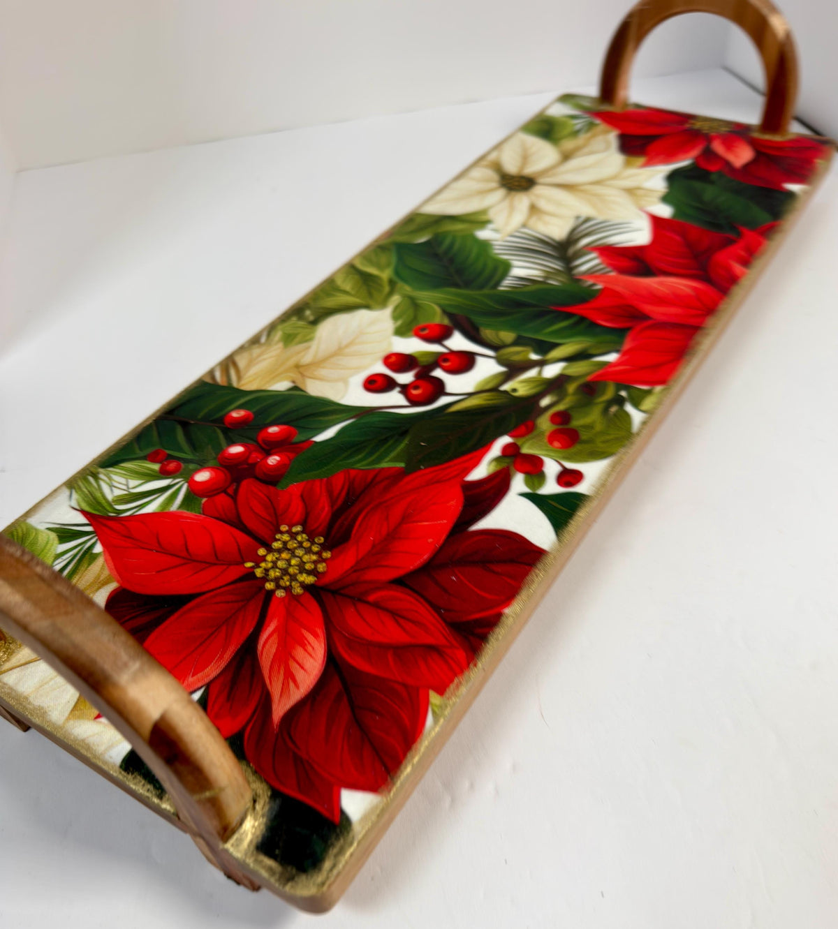 A decorative wooden tray with a floral pattern featuring red poinsettia flowers, green leaves, and red berries.