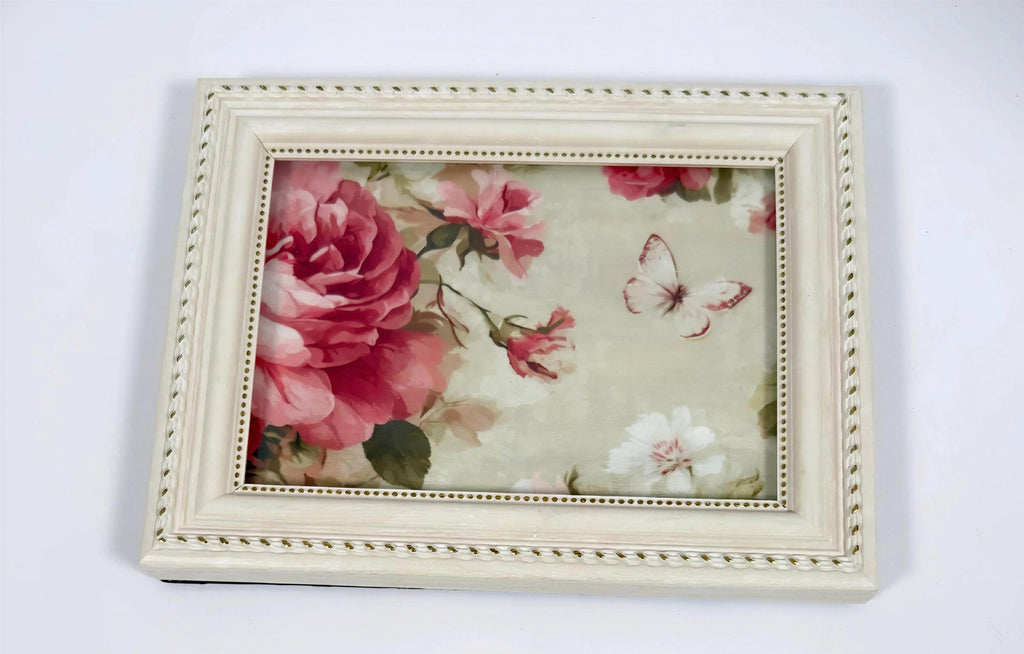 a white picture frame with a floral design, containing a large pink flower and a butterfly.