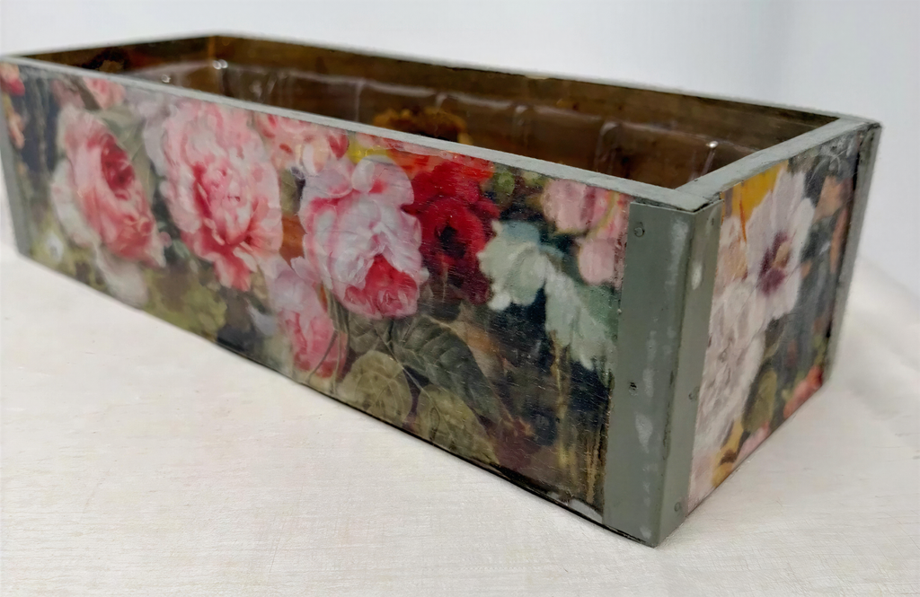 A rectangular wooden box with a floral pattern painted on it, featuring a variety of pink and red flowers.