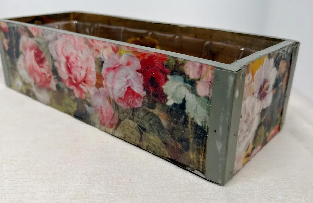 A rectangular wooden box with a floral pattern painted on it, featuring a variety of pink and red flowers.