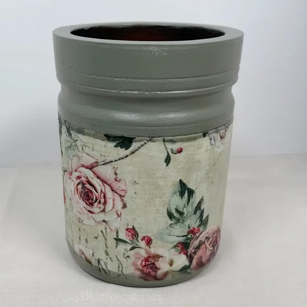 A gray vase with a floral pattern on it, sitting on a white surface.