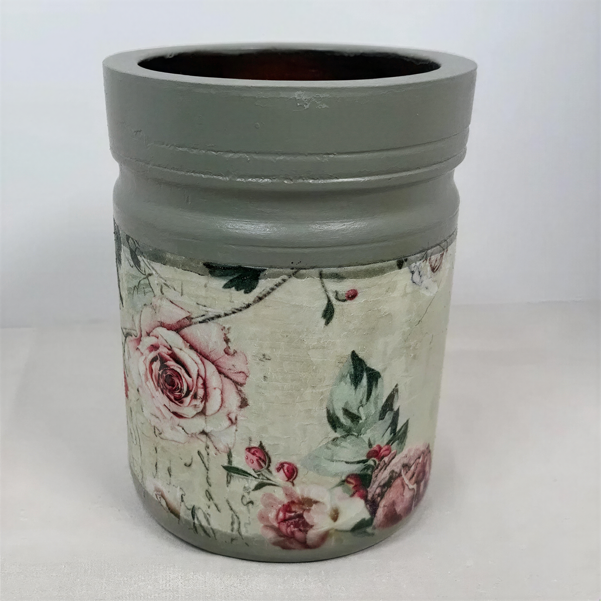 A gray vase with a floral pattern on it, sitting on a white surface.