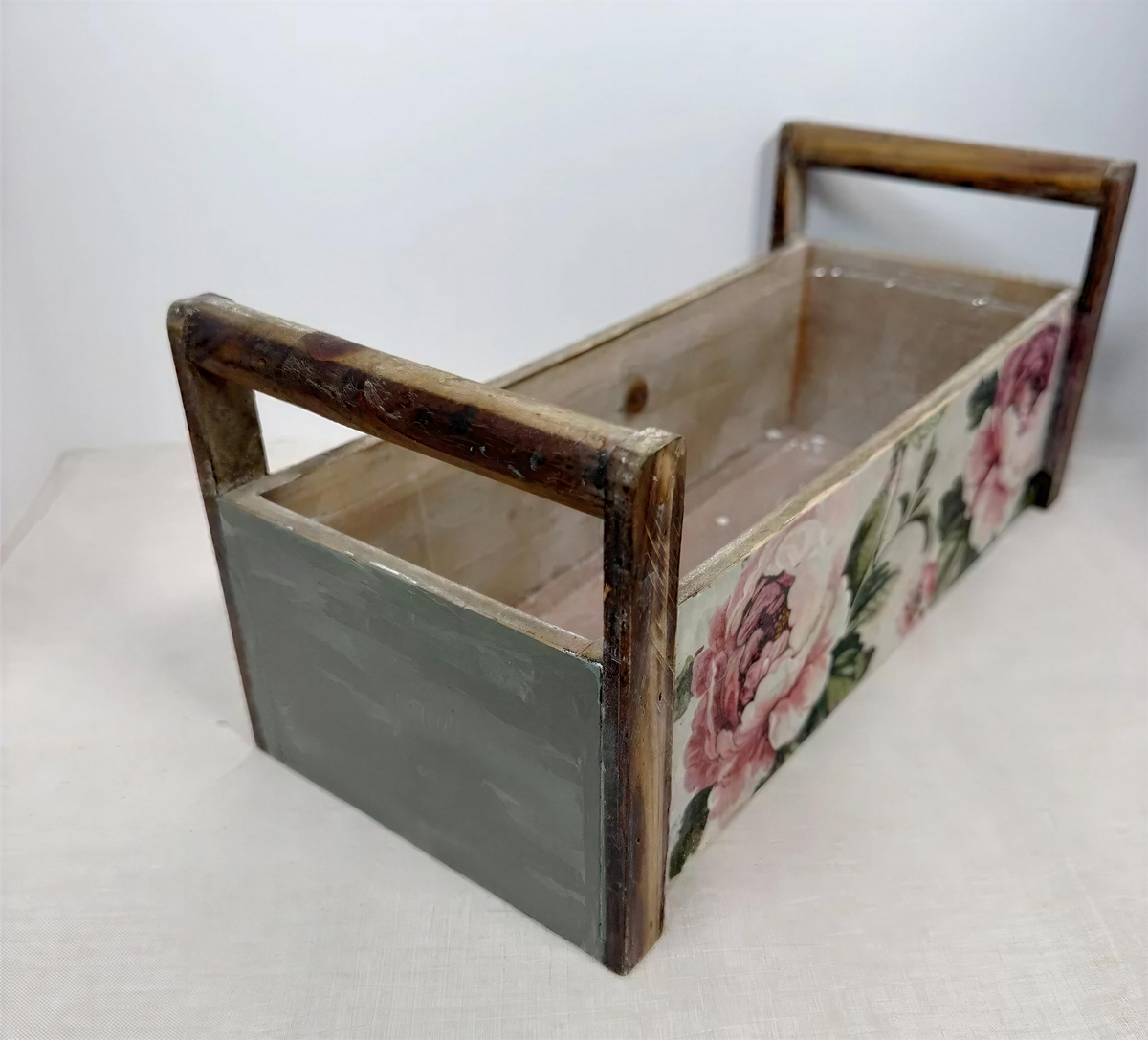 A wooden box with a floral pattern on the side, featuring a green and brown color scheme.