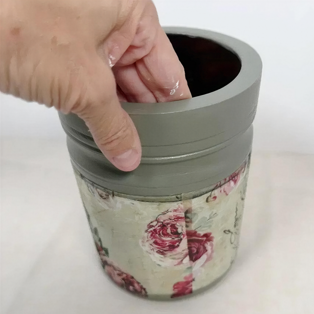 A hand is pressing down on the rim of a gray container with a floral pattern.