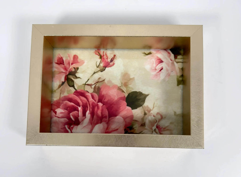 A gold-framed picture frame containing a floral print of pink and red roses.