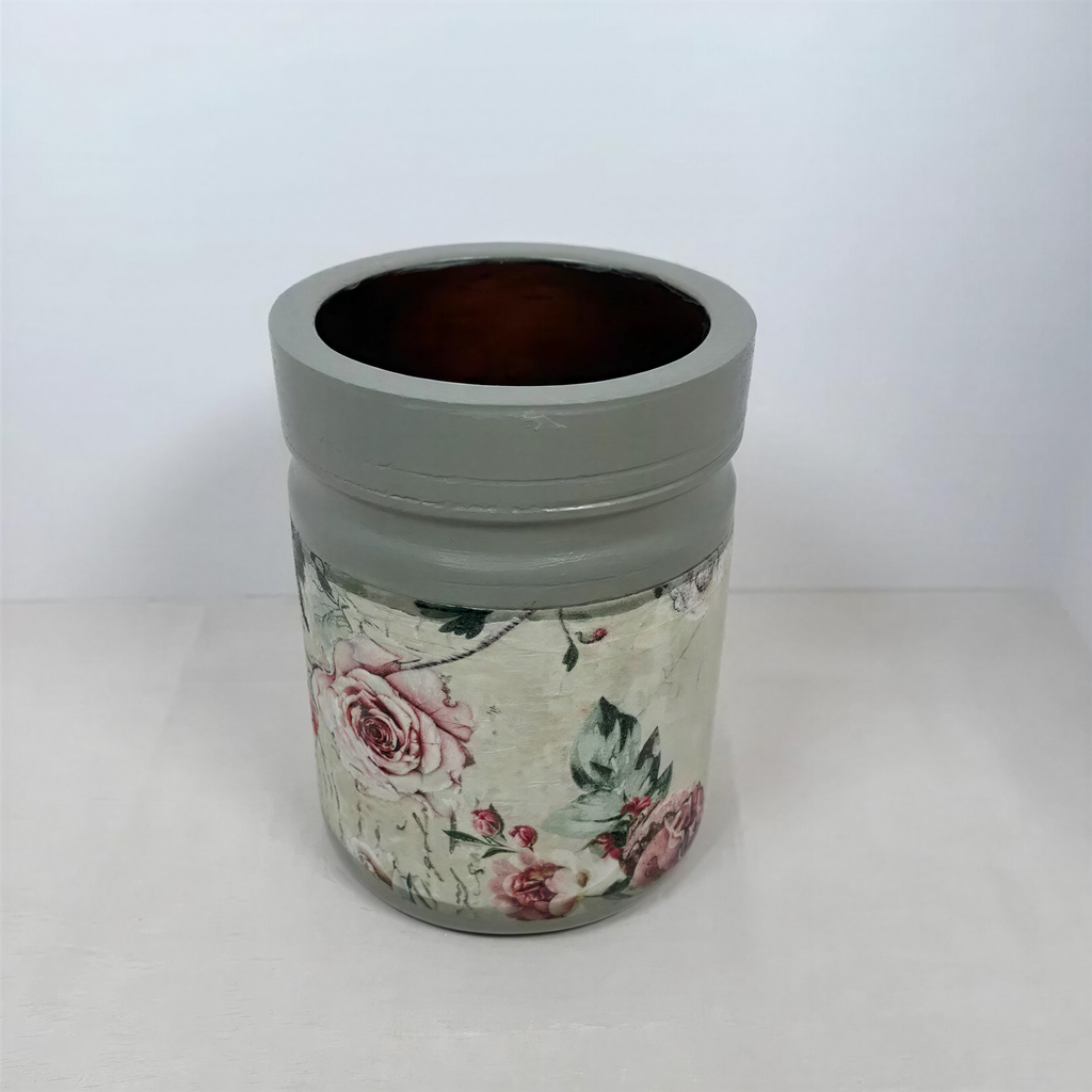 A gray vase with a floral pattern on it, sitting on a white surface.