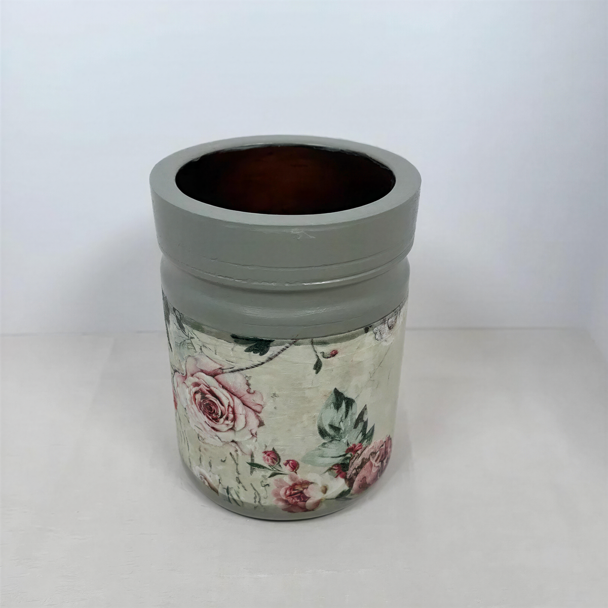 A gray vase with a floral pattern on it, sitting on a white surface.
