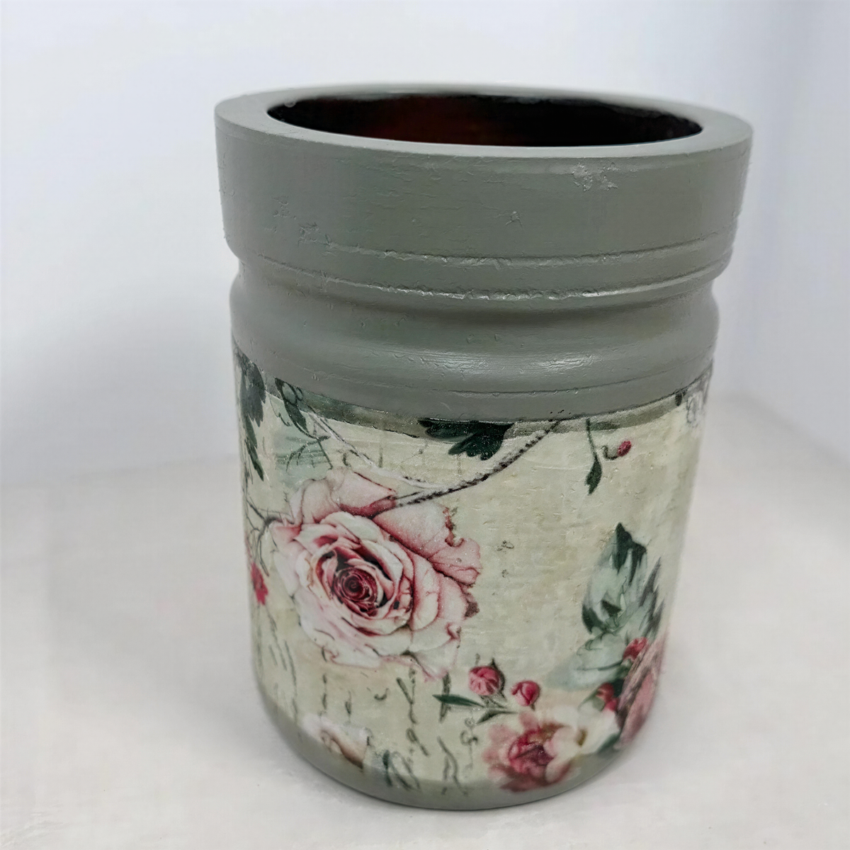 A gray vase with a floral pattern on it, sitting on a white surface.