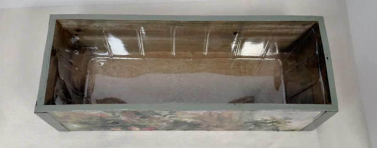 a wooden box with a floral pattern on the front, sitting on a white surface.