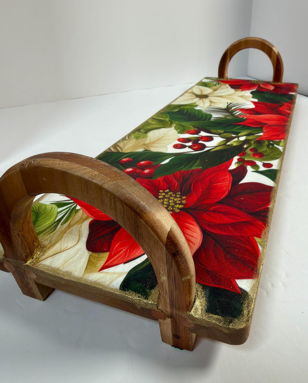 A wooden serving tray with a vibrant floral design featuring red poinsettia flowers, green leaves, and red berries.