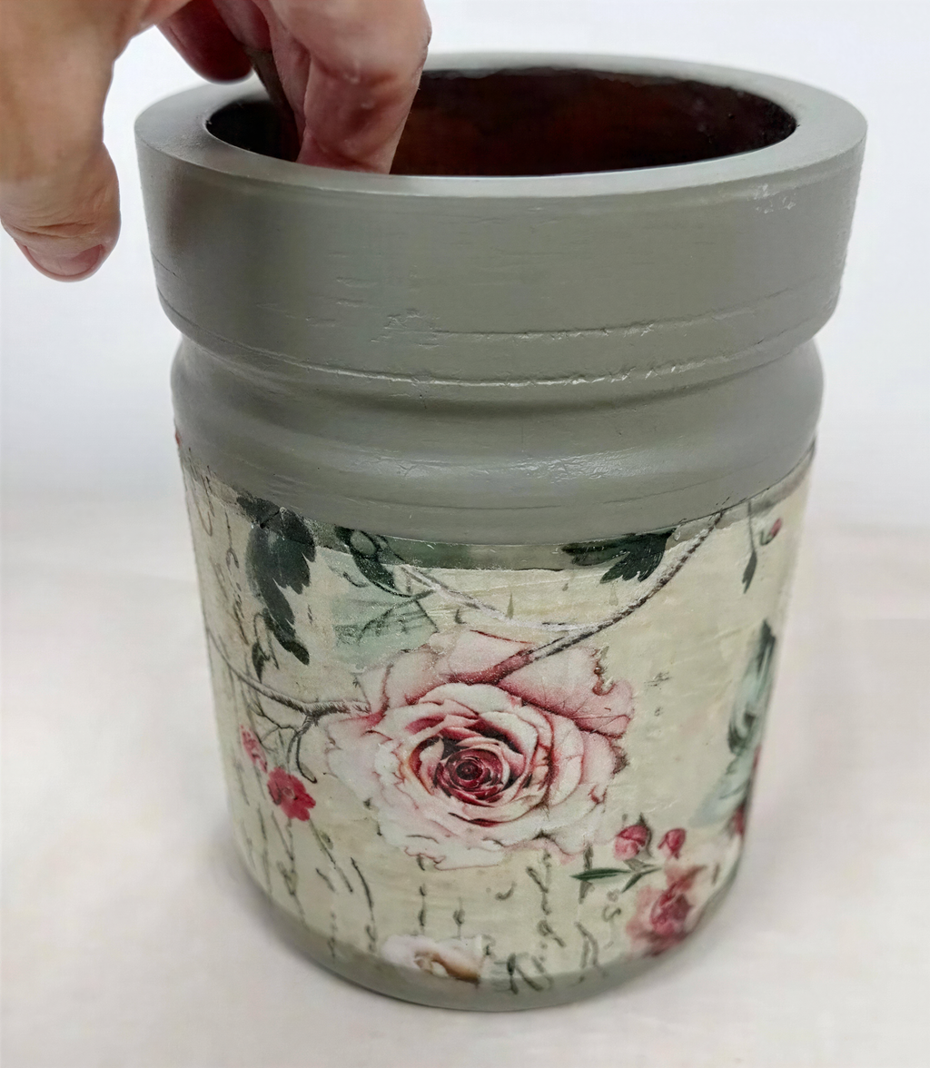 A hand is holding a gray vase with a floral pattern on it, which appears to be a decorative piece.