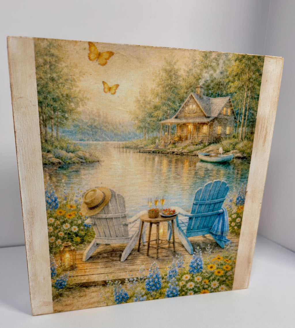 A painting depicting a serene lakeside scene with a cabin, two chairs, and a table, surrounded by flowers and butterflies.