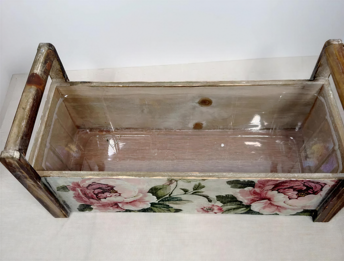 a wooden box with a floral pattern on the front, sitting on a white surface.