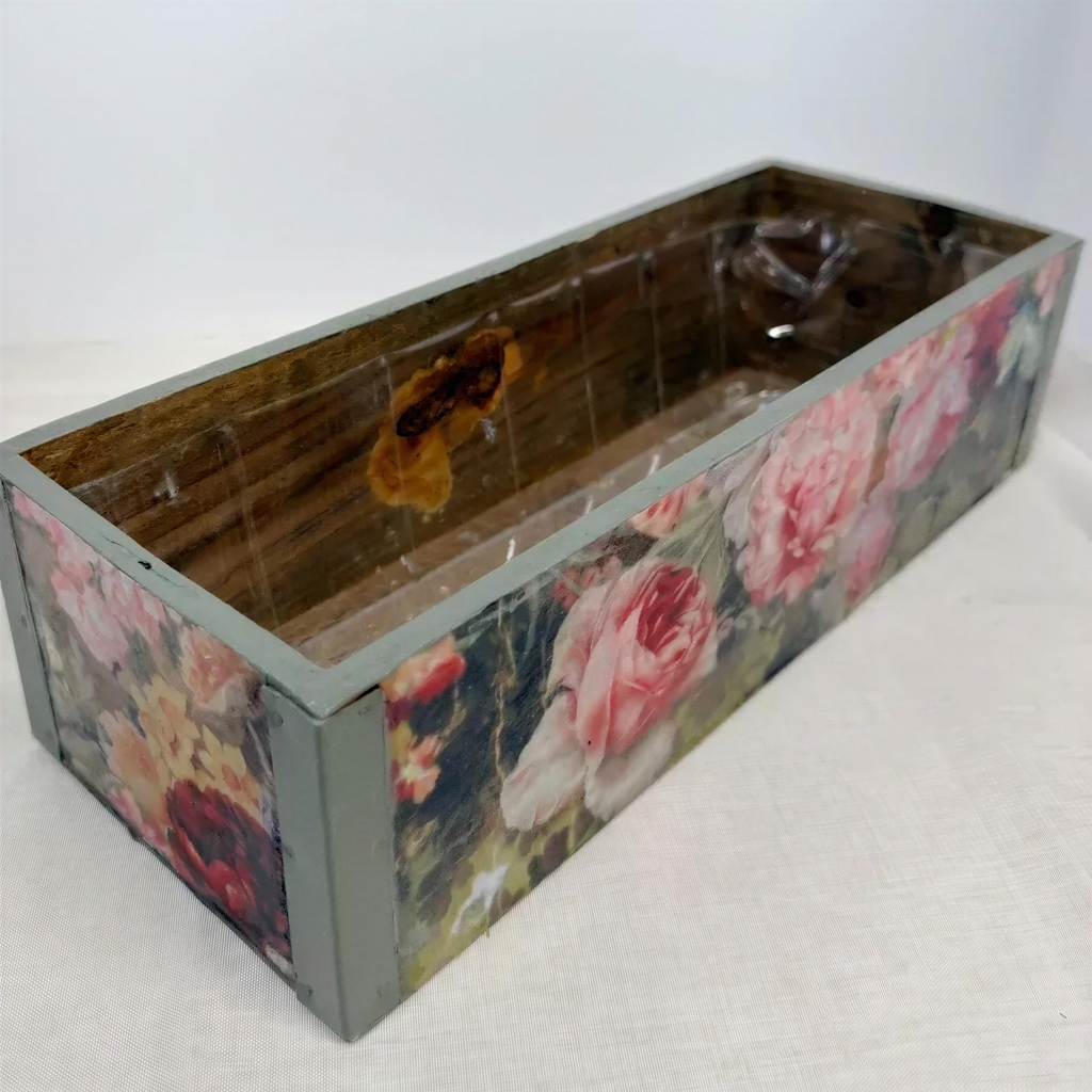 A wooden box with a floral pattern on its side, sitting on a white surface.