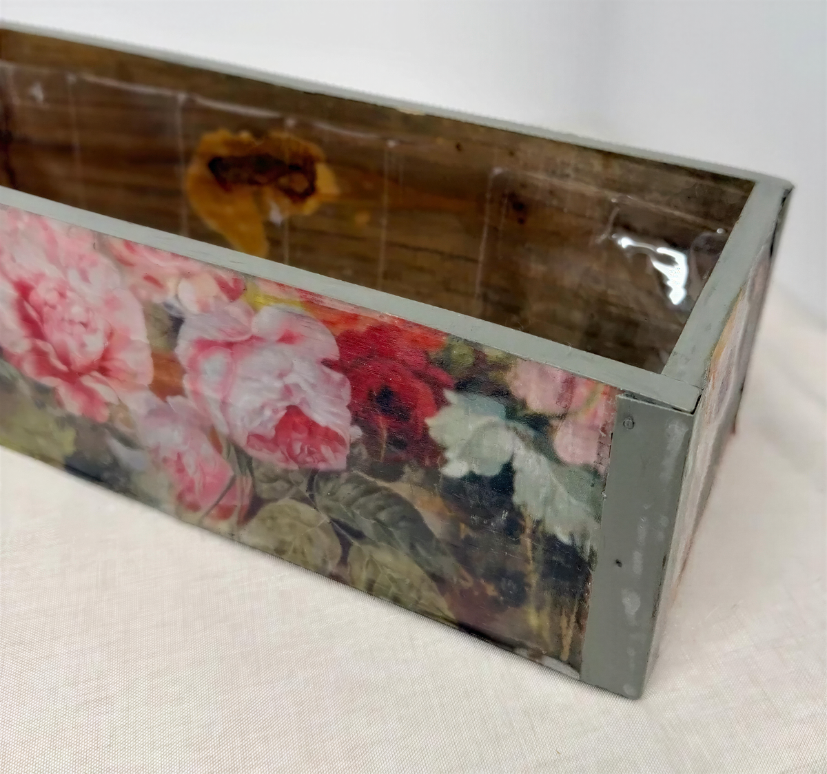 A wooden box with a floral pattern painted on it, sitting on a white surface.