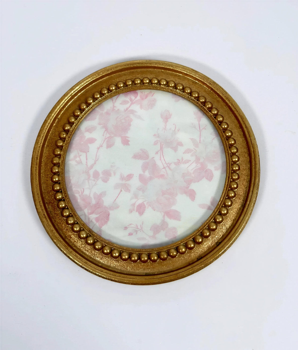 a round gold-colored frame with a floral pattern inside, set against a white background.