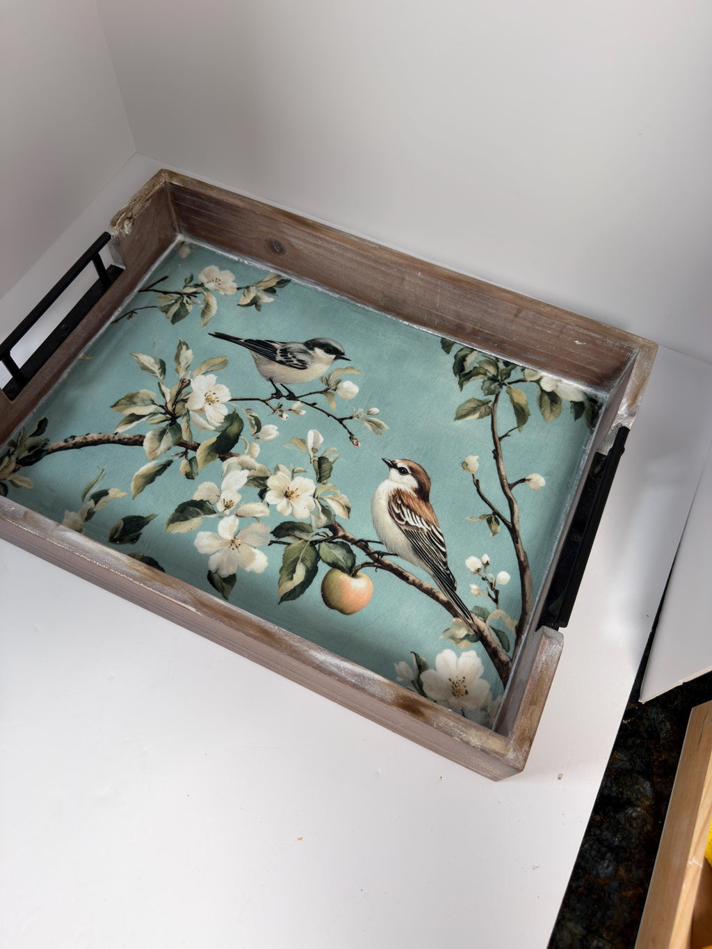 A wooden tray with a floral pattern of birds perched on branches and flowers, placed on a white surface.