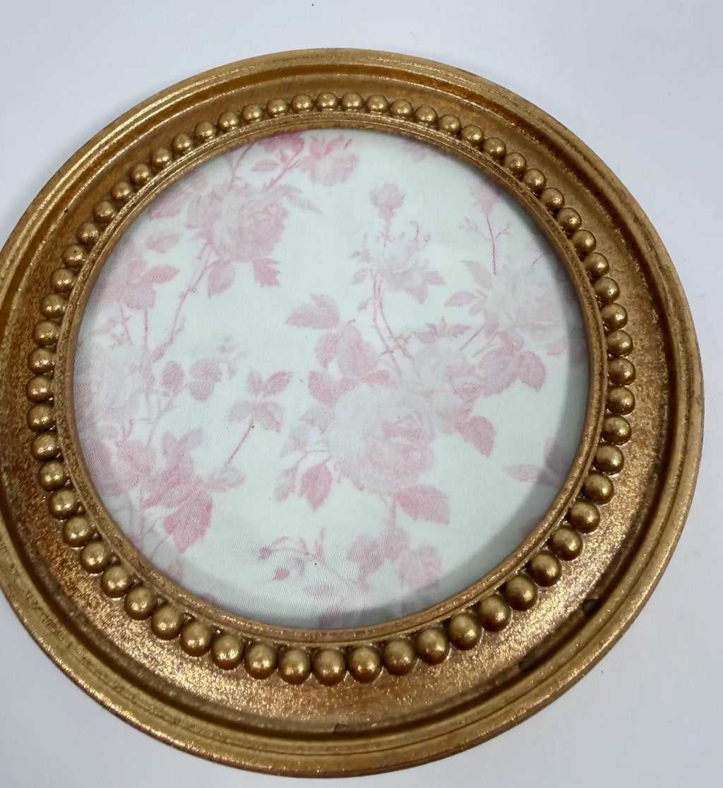 A round gold-colored frame with a floral pattern inside, placed on a white surface.