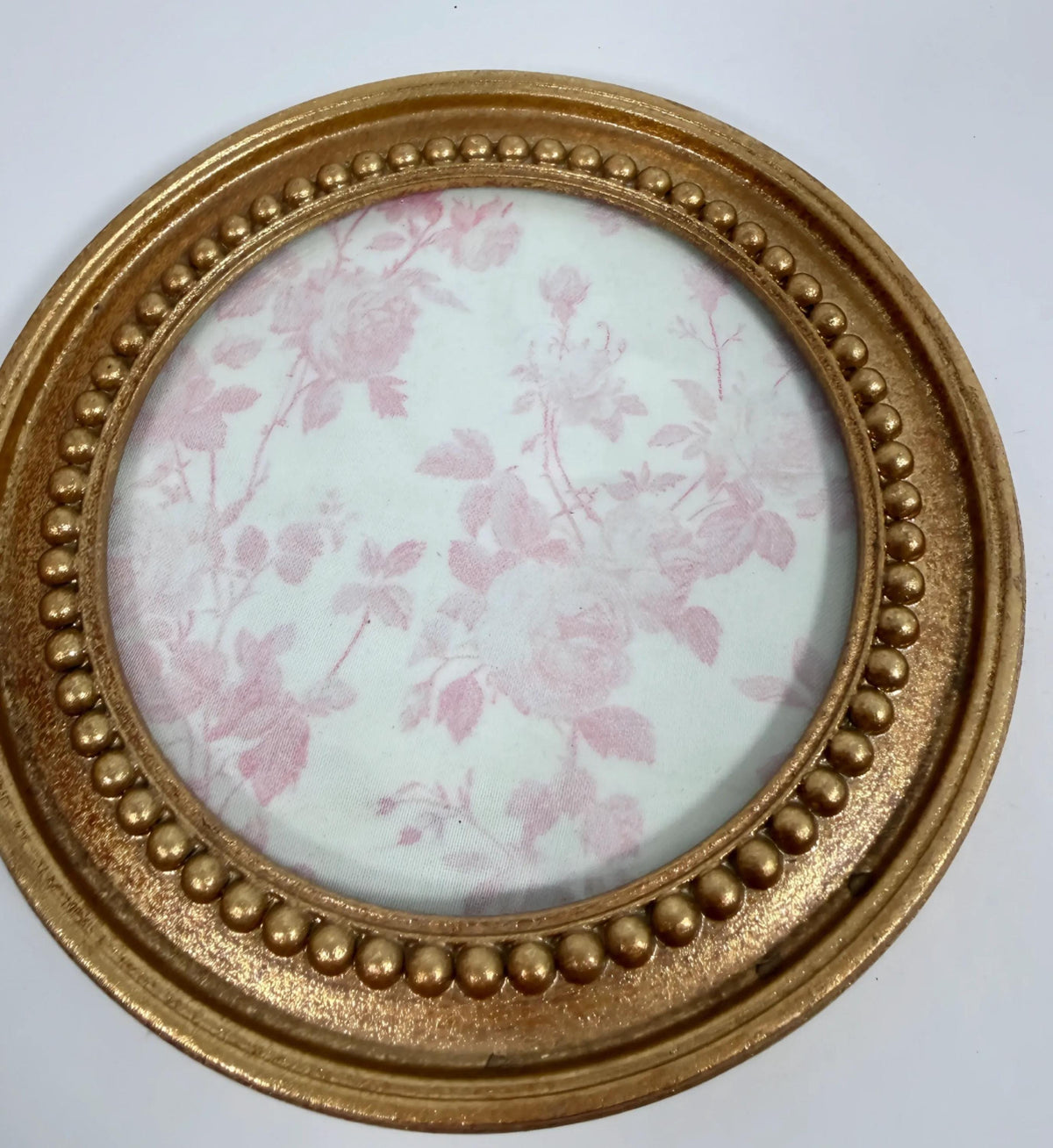 A round gold-colored frame with a floral pattern inside, placed on a white surface.