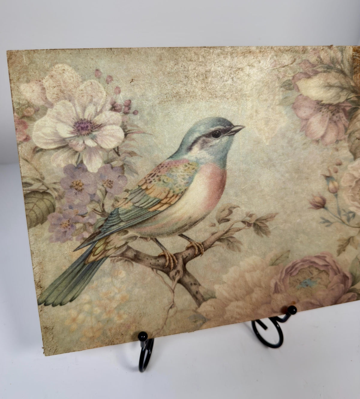 a vintage-style painting of a colorful bird perched on a branch, surrounded by flowers and foliage.